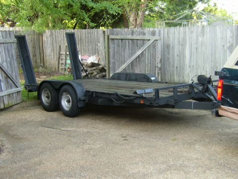 1995 Ford Bronco - A car trailer with dual axles and ramps is parked on a concrete surface in front of a wooden fence.