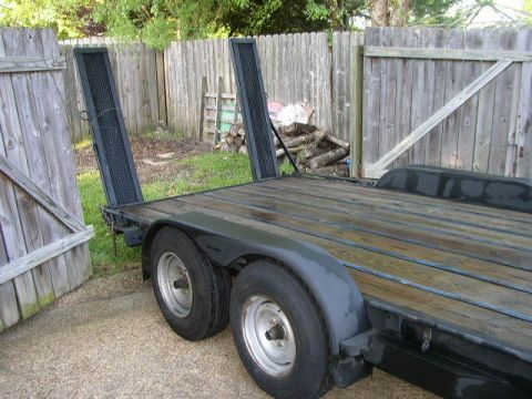1995 Ford Bronco - A trailer with a wooden deck and metal ramps is shown parked next to a wooden fence.