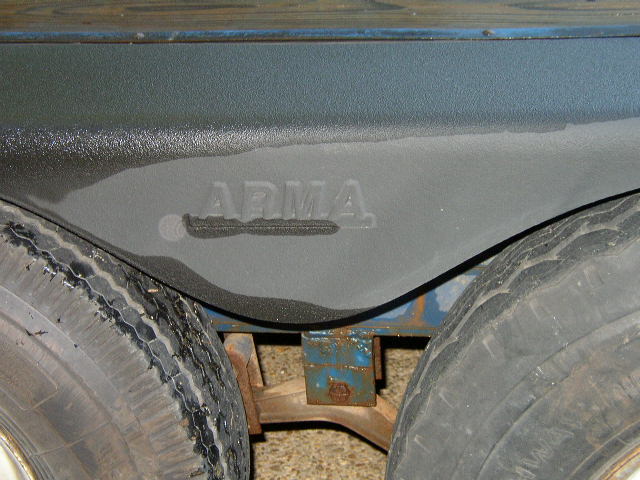 Trailer wheel well with "ARMA" embossed, showing dual tires and suspension