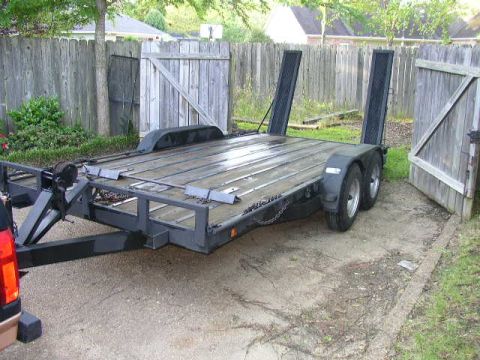 1995 Ford Bronco - A car hauler trailer is shown parked outdoors next to a wooden fence.