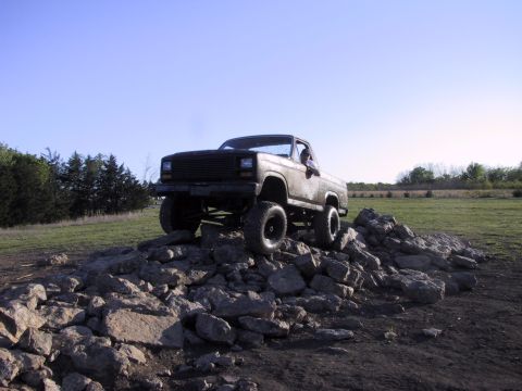1983 Ford Bronco - A lifted pickup truck navigates a rocky terrain under a clear blue sky.