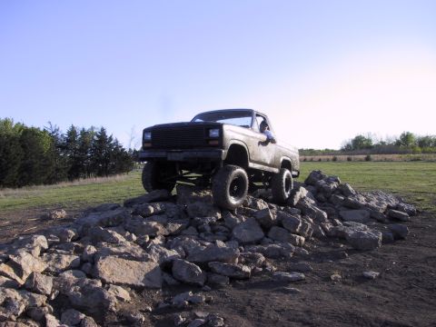 1983 Ford Bronco - This lifted pickup truck navigates a rocky obstacle course under a clear blue sky.