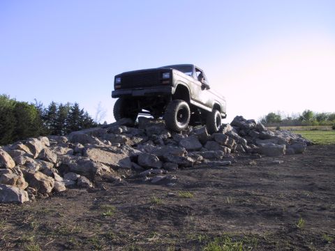 1983 Ford Bronco - A modified pickup truck navigates a rocky obstacle course under a clear blue sky.