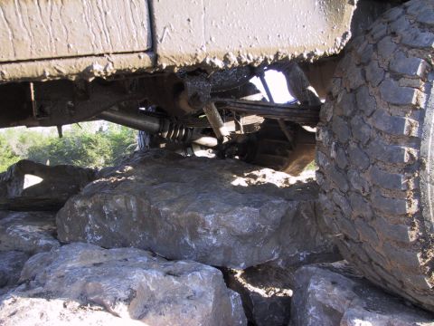 1983 Ford Bronco - An off-road vehicle navigates a rocky terrain, with its undercarriage and tire prominently displayed.