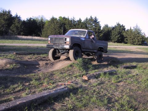 1983 Ford Bronco - A modified pickup truck navigates a dirt track with logs and uneven terrain.