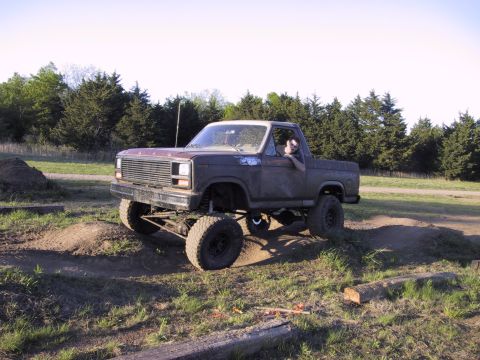1983 Ford Bronco - A lifted 1980s Ford F-Series truck navigates an off-road course with a driver visible.