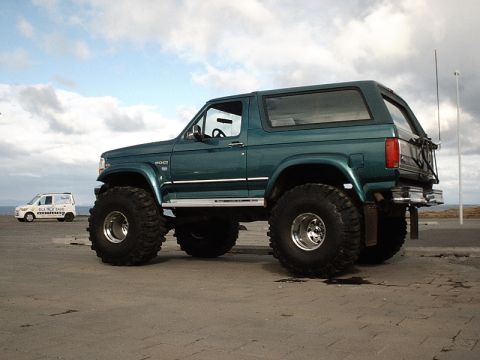 1996 Ford Bronco - A lifted green 1996 Ford Bronco sits on a paved surface under a cloudy sky, with a white van in the background.