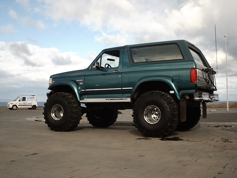 Lifted teal Ford Bronco on oversized tires, side view, on paved coastal lot