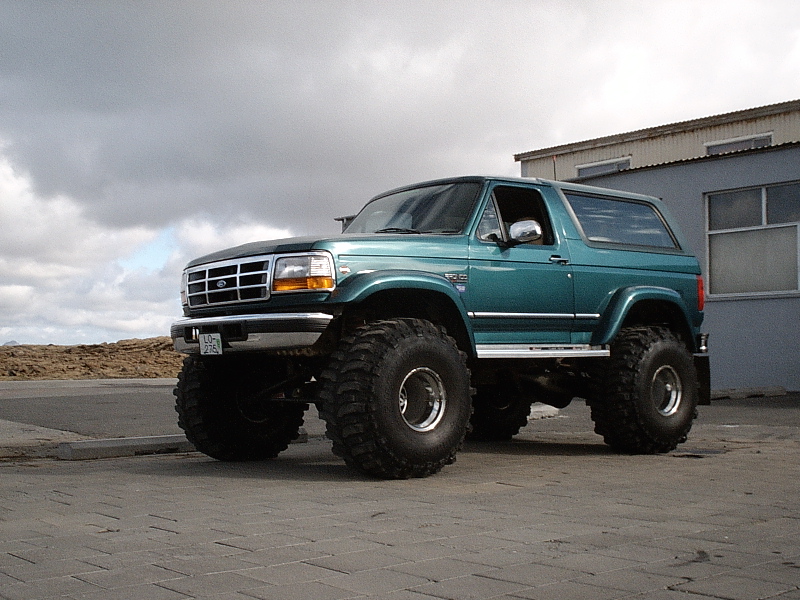 Teal lifted two-door Ford Bronco SUV on large off-road tires in a paved lot