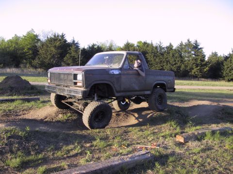 1983 Ford Bronco - A modified pickup truck is shown navigating an off-road course with a driver inside.
