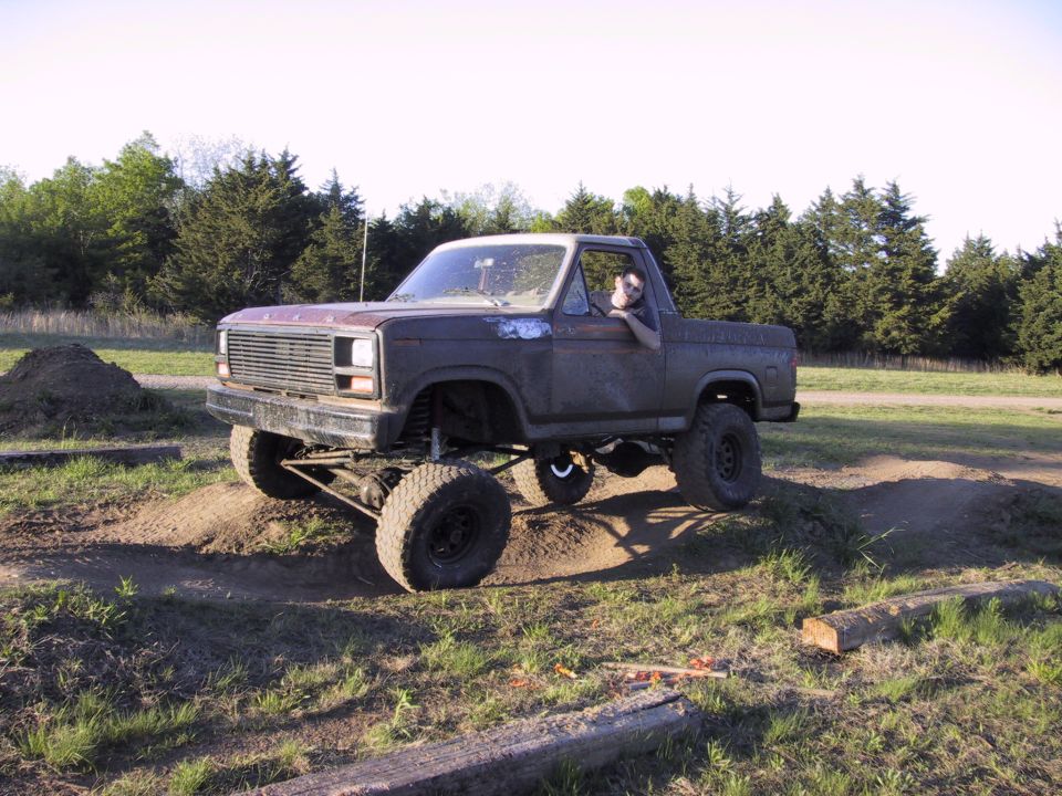 Lifted faded Ford Bronco crossing dirt whoops, front axle and steering linkage exposed