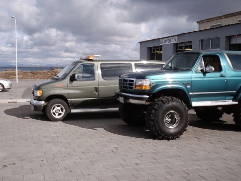 1996 Ford Bronco - Two modified SUVs, a 1996 Ford Bronco and a van, are parked side-by-side on a paved area.