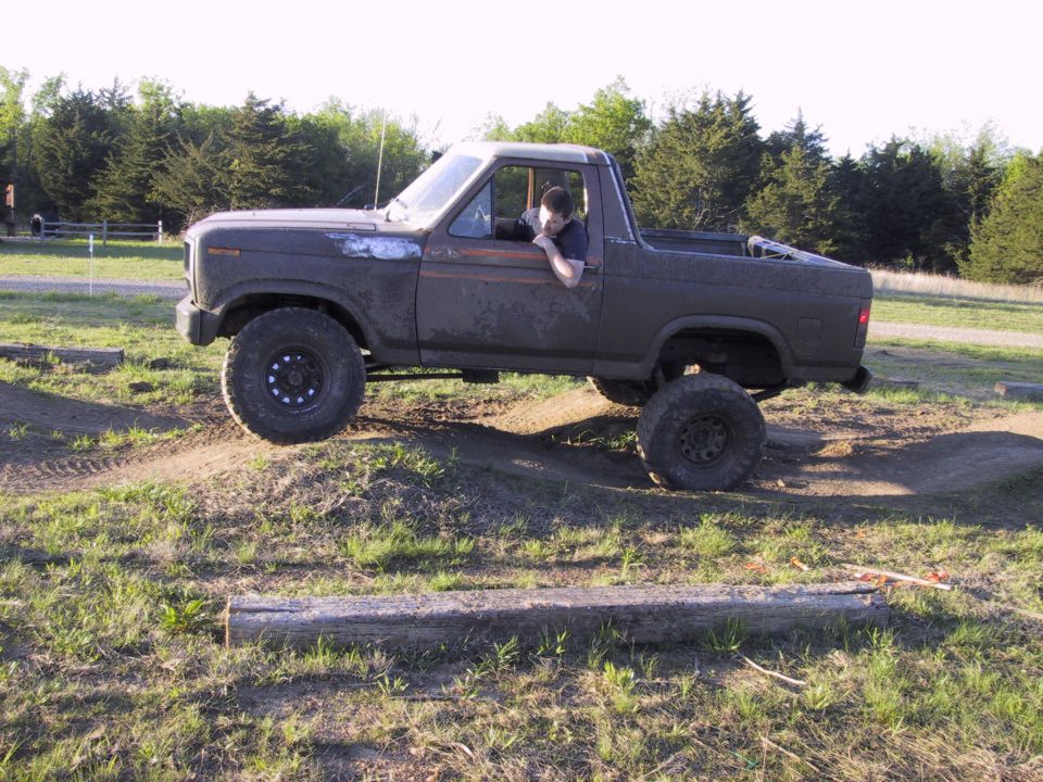 Lifted topless Ford Bronco on dirt whoops in a grass field, driver leaning out window
