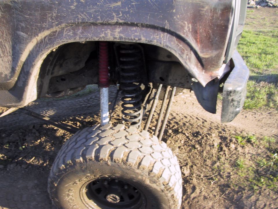 Drooped front suspension of lifted 4x4 with extended coil spring, red-boot shock and steel wheel
