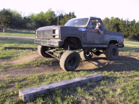 1983 Ford Bronco - A heavily modified pickup truck sits on uneven terrain under a bright sky.