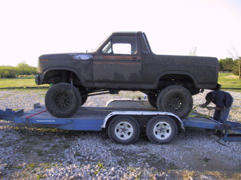1983 Ford Bronco - A person secures a lifted Bronco onto a trailer, preparing it for transport.