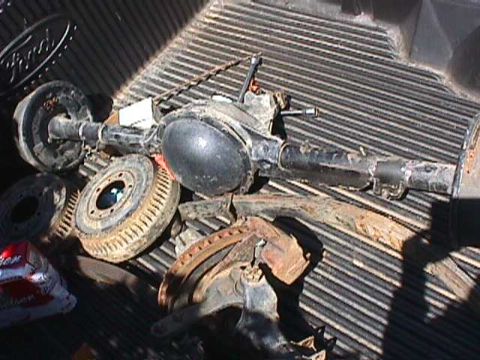1984 Jeep Wrangler - Various automotive parts, including a rear axle and brake components, are piled in the bed of a pickup truck.