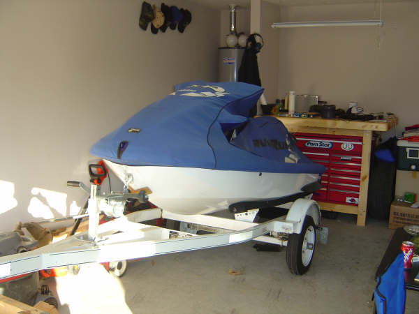 Covered blue personal watercraft on white trailer in a garage