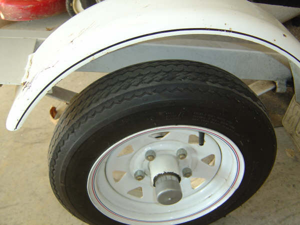 White trailer wheel and tire with white spoke rim and gray hub cap under a white fender
