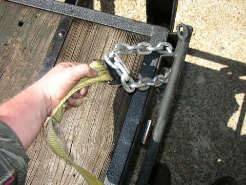 1995 Ford Bronco - A hand is shown securing a strap to a chain on a trailer, likely for transport.