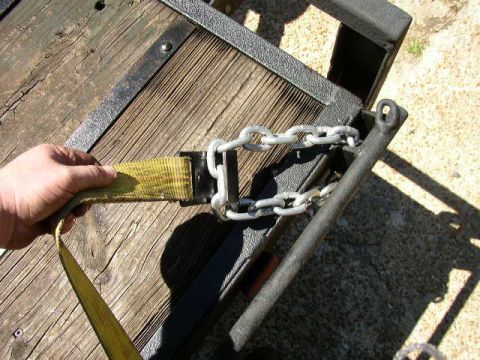 1995 Ford Bronco - A hand secures a tie-down strap and chain to a trailer or vehicle frame.