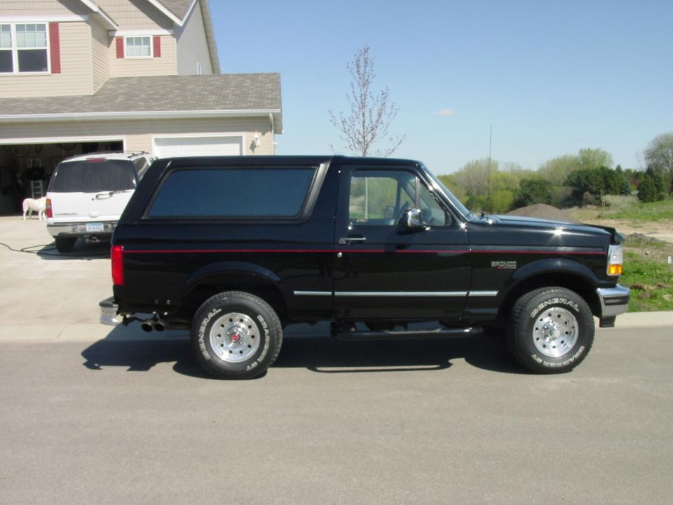 Black Ford Bronco SUV with red pinstripe, side view, parked in a suburban driveway