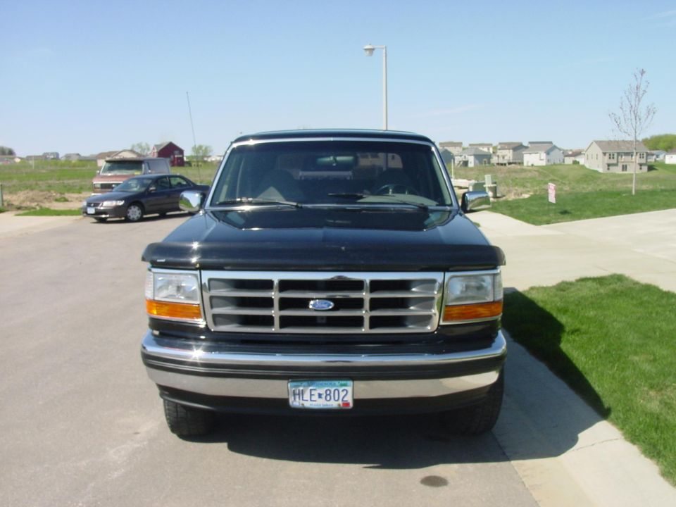Front of black Ford F-series with chrome grille and Minnesota plate HLE-802 in a driveway