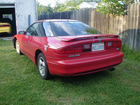 1993 Ford Probe - A red 1993 Ford Probe is parked on the grass, with a yellow car visible in the background garage.