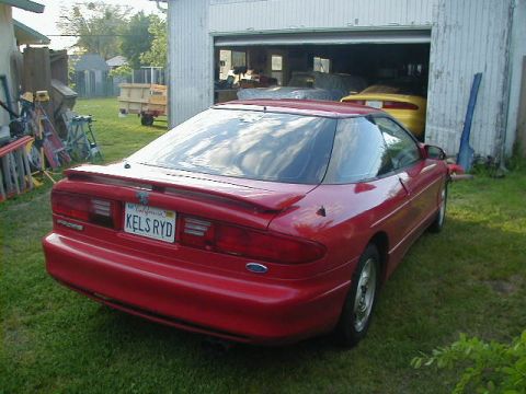 1993 Ford Probe - A red 1993 Ford Probe is parked in front of a garage, with another car visible inside.