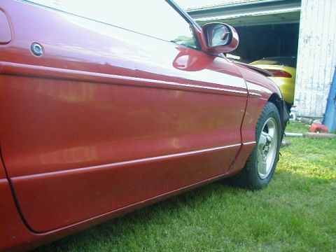 1993 Ford Probe - Side view of a red 1993 Ford Probe, with another yellow vehicle in the background.