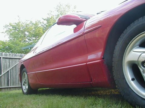 1993 Ford Probe - A red coupe is shown from the side, parked on a grassy lawn with a wooden fence in the background.