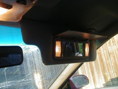 1993 Ford Probe - Interior shot of a car's visor with illuminated vanity mirror, showing a cracked windshield and a side mirror.