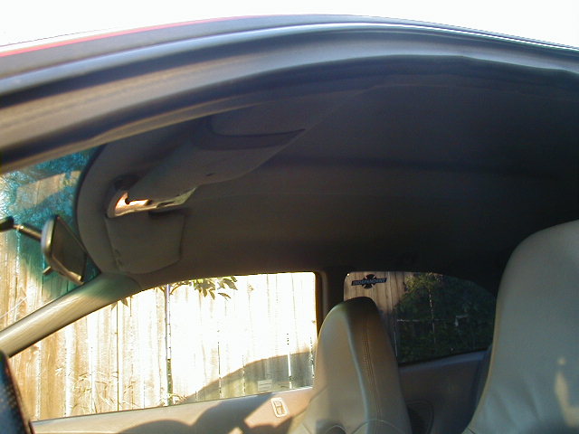 Car interior showing headliner, sun visor, and part of a seat. A sticker is visible on the rear window