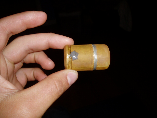 Wooden fuel tank cap with silver band and gray sealant, held in a hand