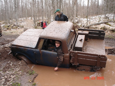 1969 International Scout 800a - A group of people watch as a pickup truck is stuck deep in the mud.