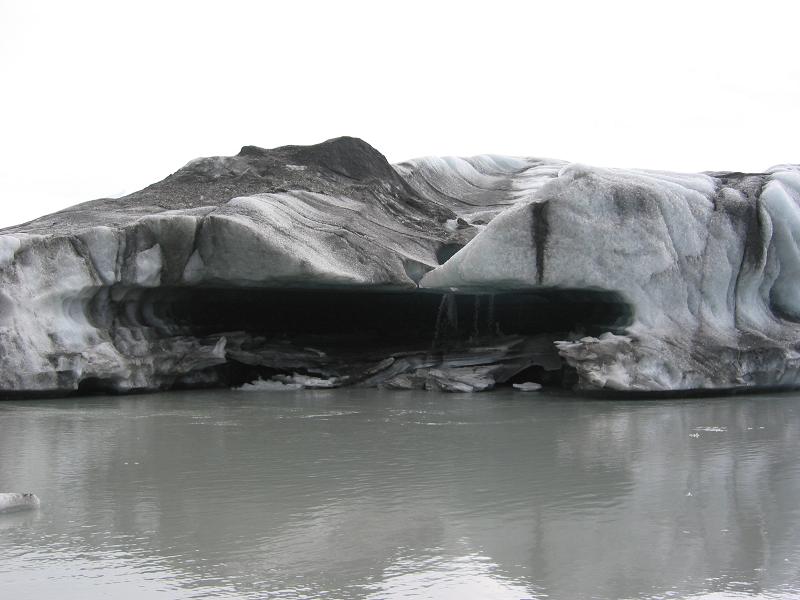 Dirt-streaked glacier face with a dark melt cavity above gray meltwater
