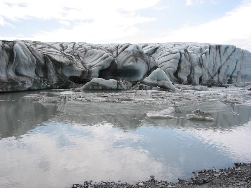 Crevassed gray glacier wall above a meltwater lagoon with floating ice