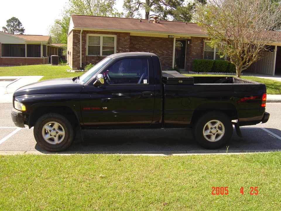 Black Dodge Ram 1500 pickup driver-side profile parked at curb by brick house