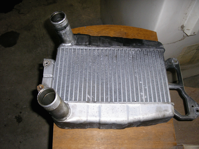 Aluminum intercooler with two ports resting on a wooden chair