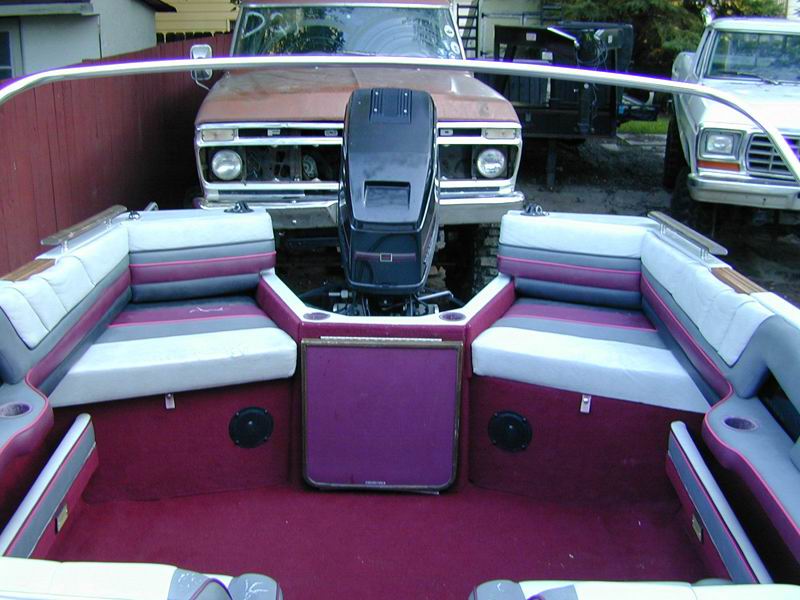 Boat cockpit with purple and gray seating, outboard motor, classic Ford trucks behind