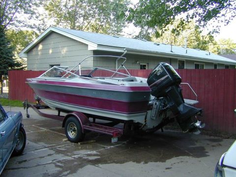 1989 Maxum 2000/XC - A boat is parked on a trailer in front of a house and a red fence.