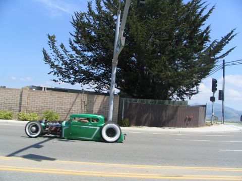 1986 Pontiac Fiero - A green hot rod coupe is seen driving on the road with custom trim and white wall tires.