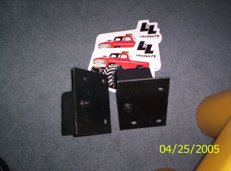 Two black metal brackets on a gray carpeted surface with two stickers of red trucks and the date 04/25/2005