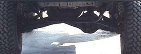 1990 Ford Bronco - Low-angle view beneath a vehicle between two large tires showing the axle, differential housing, and undercarriage.