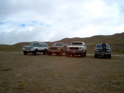 1988 Ford Bronco - A group of four SUVs are parked on a barren, grassy hillside with rolling hills in the background.