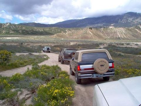 1988 Ford Bronco - A convoy of Ford Broncos travels down a dusty trail through a , mountainous landscape.