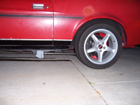 1971 Ford Mustang - Side view of a red car with a black stripe and aftermarket wheels, showing the door handle and wheel well.