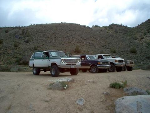 1988 Ford Bronco - A group of four-wheel-drive vehicles are parked in a line on a dusty, arid terrain under a cloudy sky.