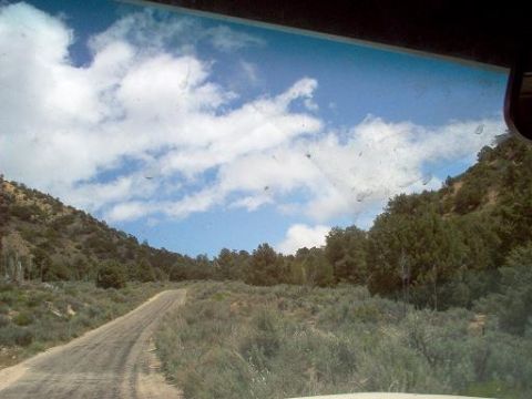 1988 Ford Bronco - A dirt road winds through a dry, brushy landscape with trees on the hillsides under a partly cloudy sky.