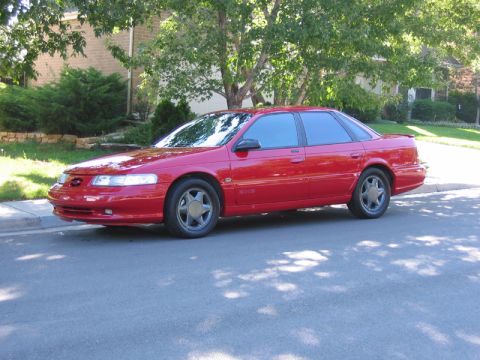 1995 Ford Taurus - This red 1995 Ford Taurus sedan is seen from a three-quarter front angle, parked on a residential street.